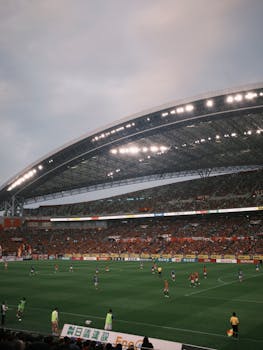 A lively soccer match in a vast, modern stadium filled with enthusiastic spectators.