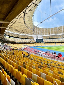 Expansive stadium interior featuring bright yellow seats and a vibrant blue athletic track with spectators.