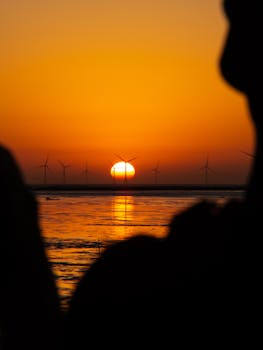 Peaceful sunset over wind turbines in Hsinchu, Taiwan, with glowing reflections on the water.