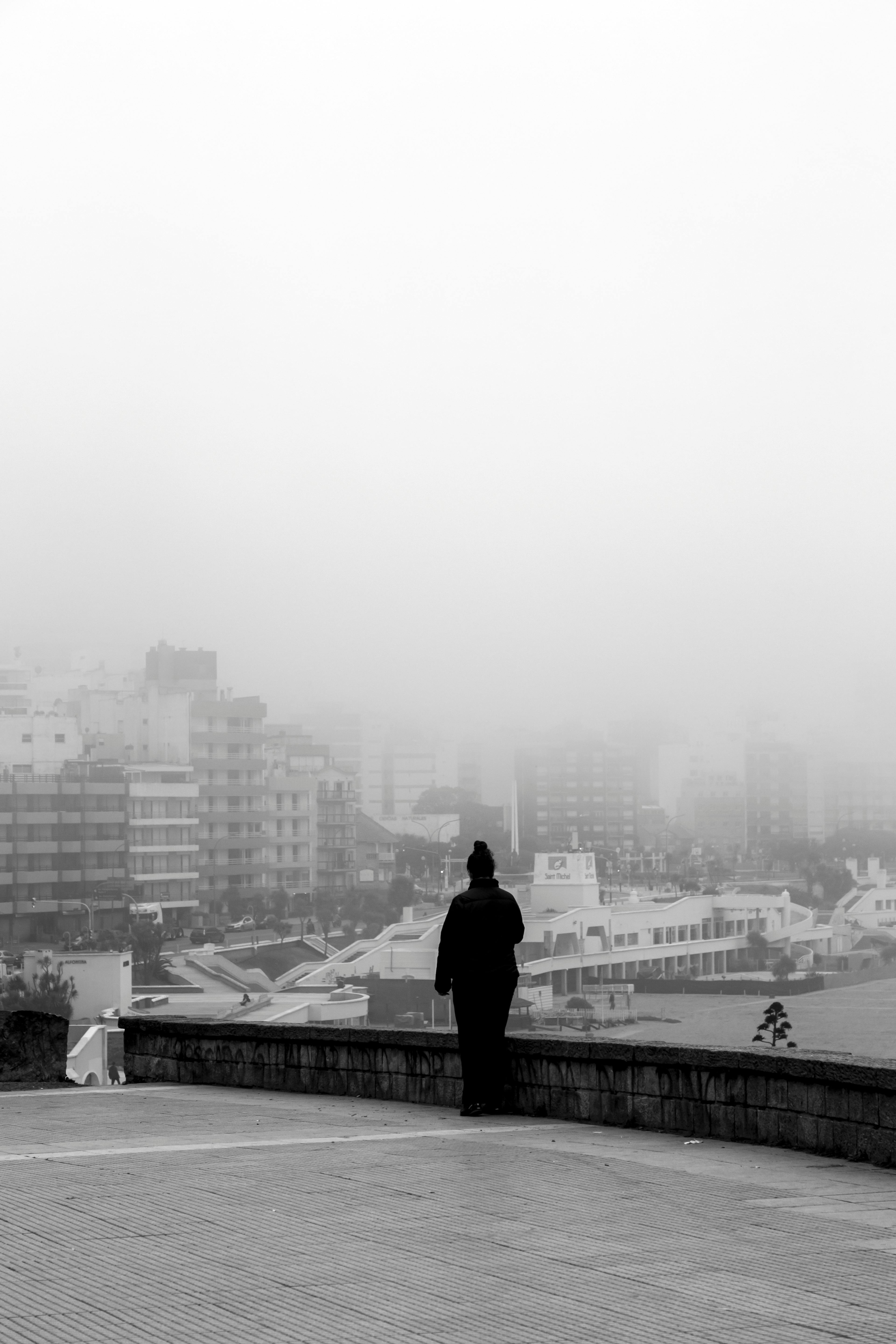 A lone figure stands overlooking a foggy cityscape in Mar del Plata, Argentina. Moody black and white photo.