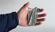 A hand holds several metal screws against a white background.
