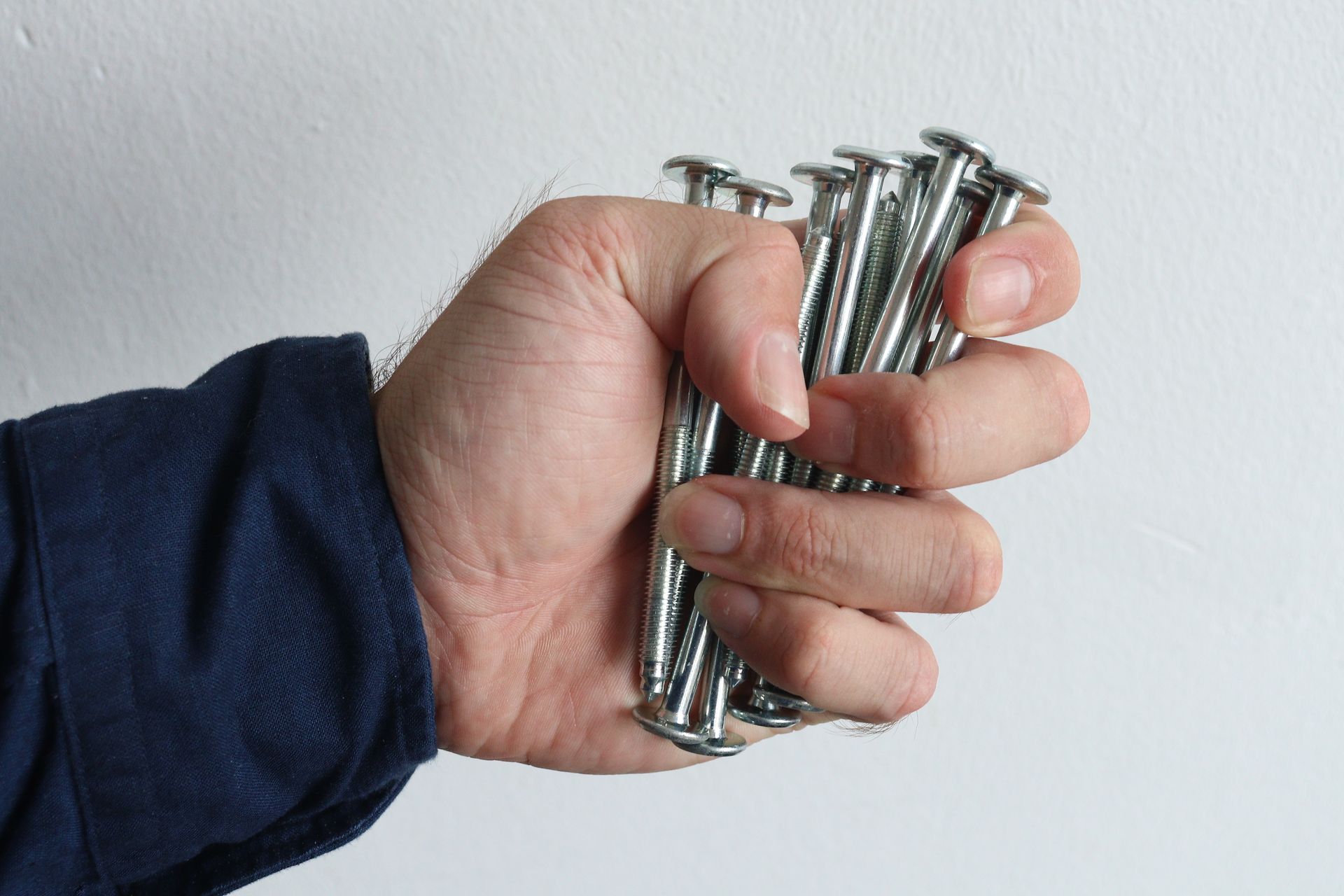 A detailed image of a hand tightly gripping shiny metal screws against a white background.