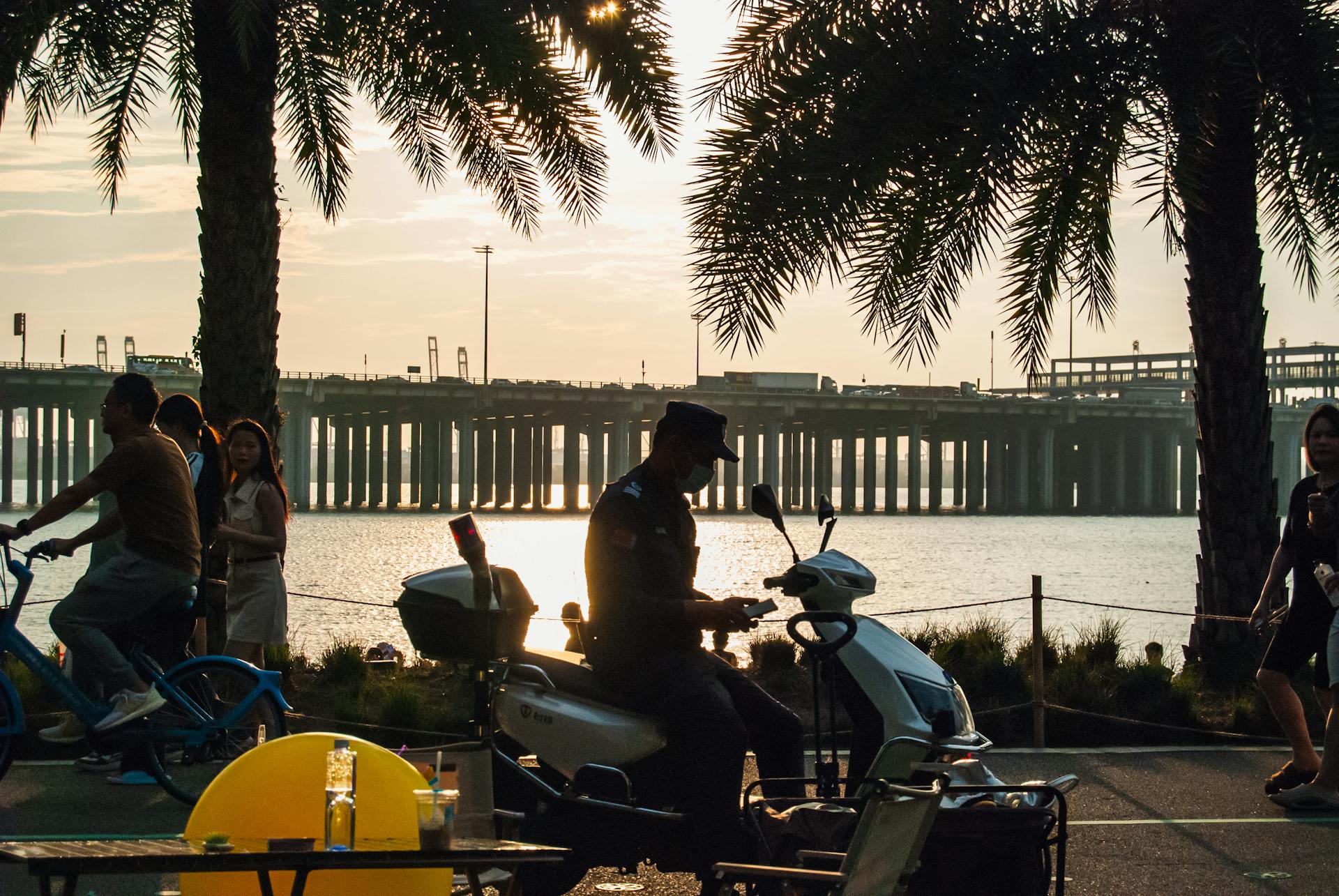 People enjoying a sunset at a park in Shenzhen by a waterfront. Silhouettes enhance the scenic view.