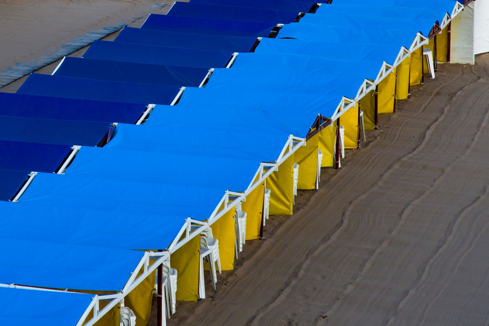 Aerial view of blue and yellow pop-up beach cabanas set up along the shoreline