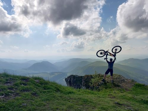 Free A mountain biker triumphantly lifts their bike atop a scenic hill with expansive views. Stock Photo