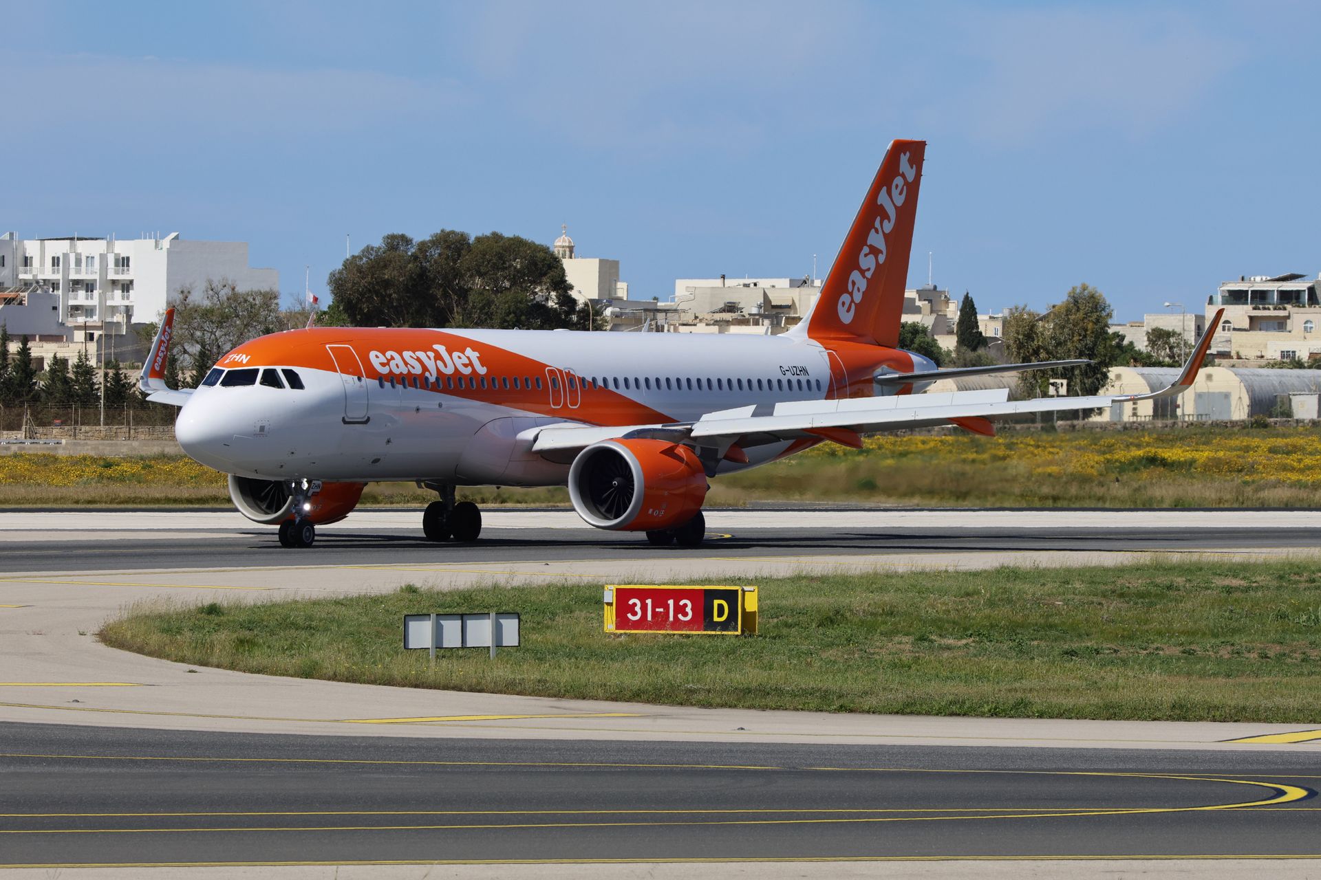 EasyJet airplane taxiing at an airport runway with buildings in the background.