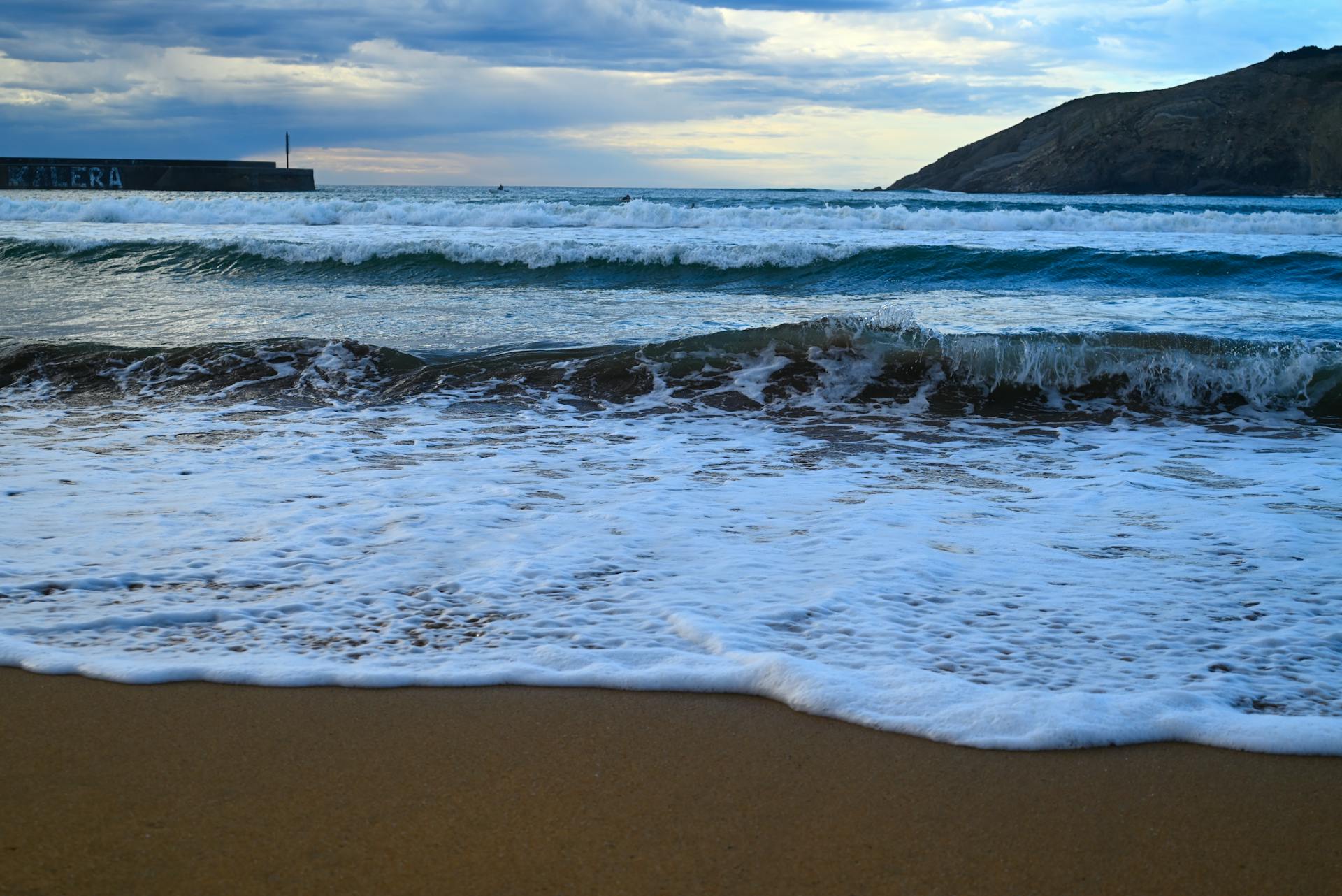 Stunning seascape of Bilbao's coast with waves crashing onto the sandy shore, captured at daybreak.