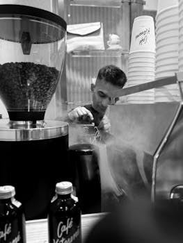 Black and white photo of a barista making coffee amidst cafe ambience.