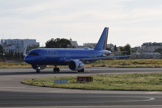 A large blue commercial airplane taxiing on a runway at a city airport under a clear sky.