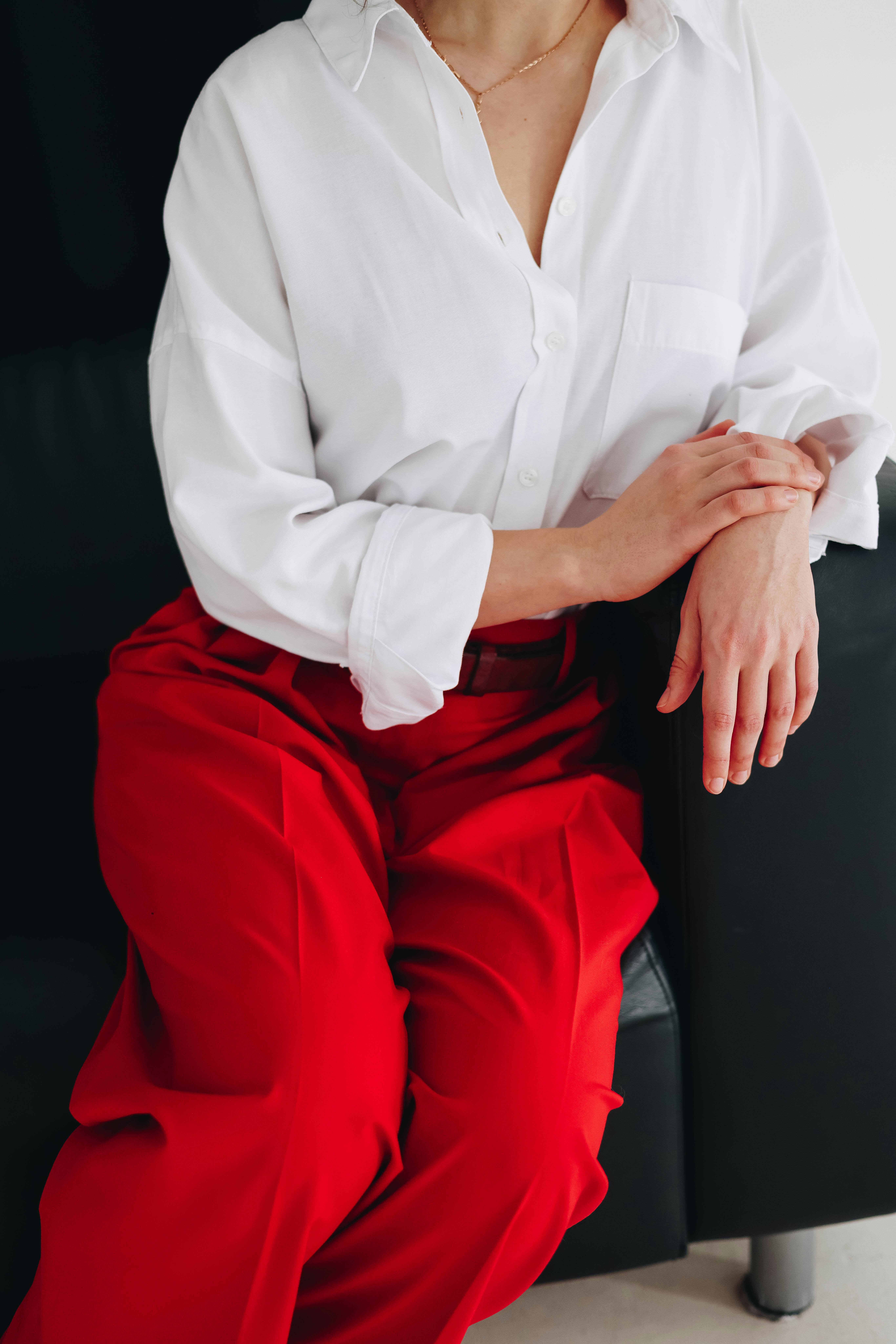 Stylish woman in white blouse and bright red pants sitting elegantly indoors.