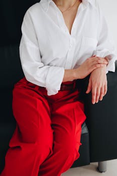 Stylish woman in white blouse and bright red pants sitting elegantly indoors.