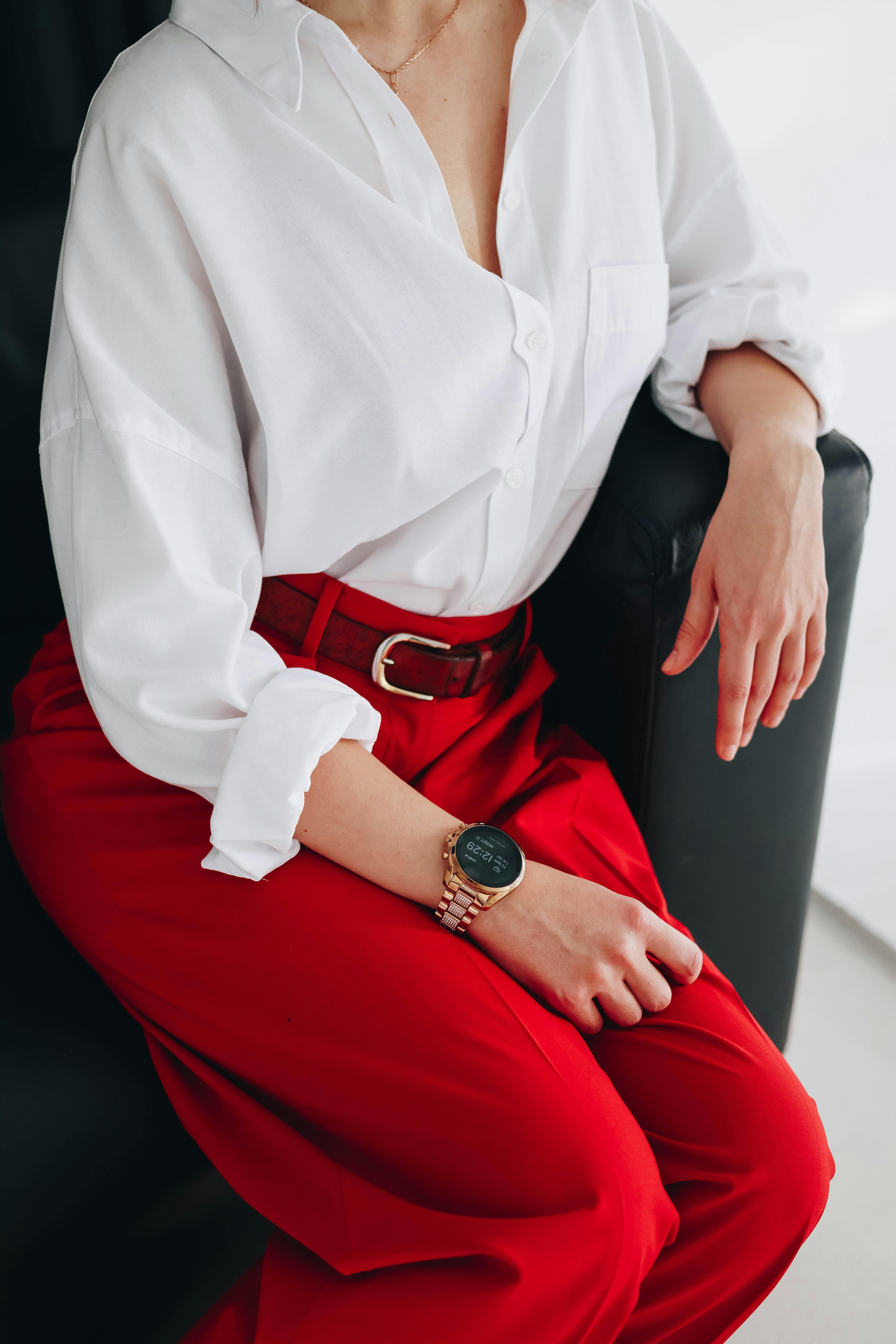 Elegant woman wearing a white shirt and red pants, seated indoors.