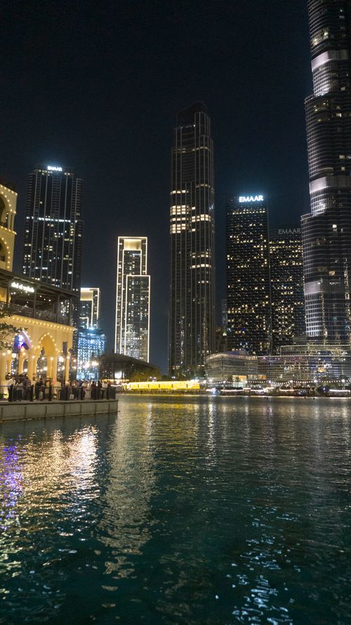 Free Nighttime cityscape of Downtown Dubai with illuminated skyscrapers reflecting on water. Stock Photo