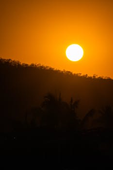 Stunning sunset landscape with a vibrant orange sky, backlighting silhouetted hills and trees.