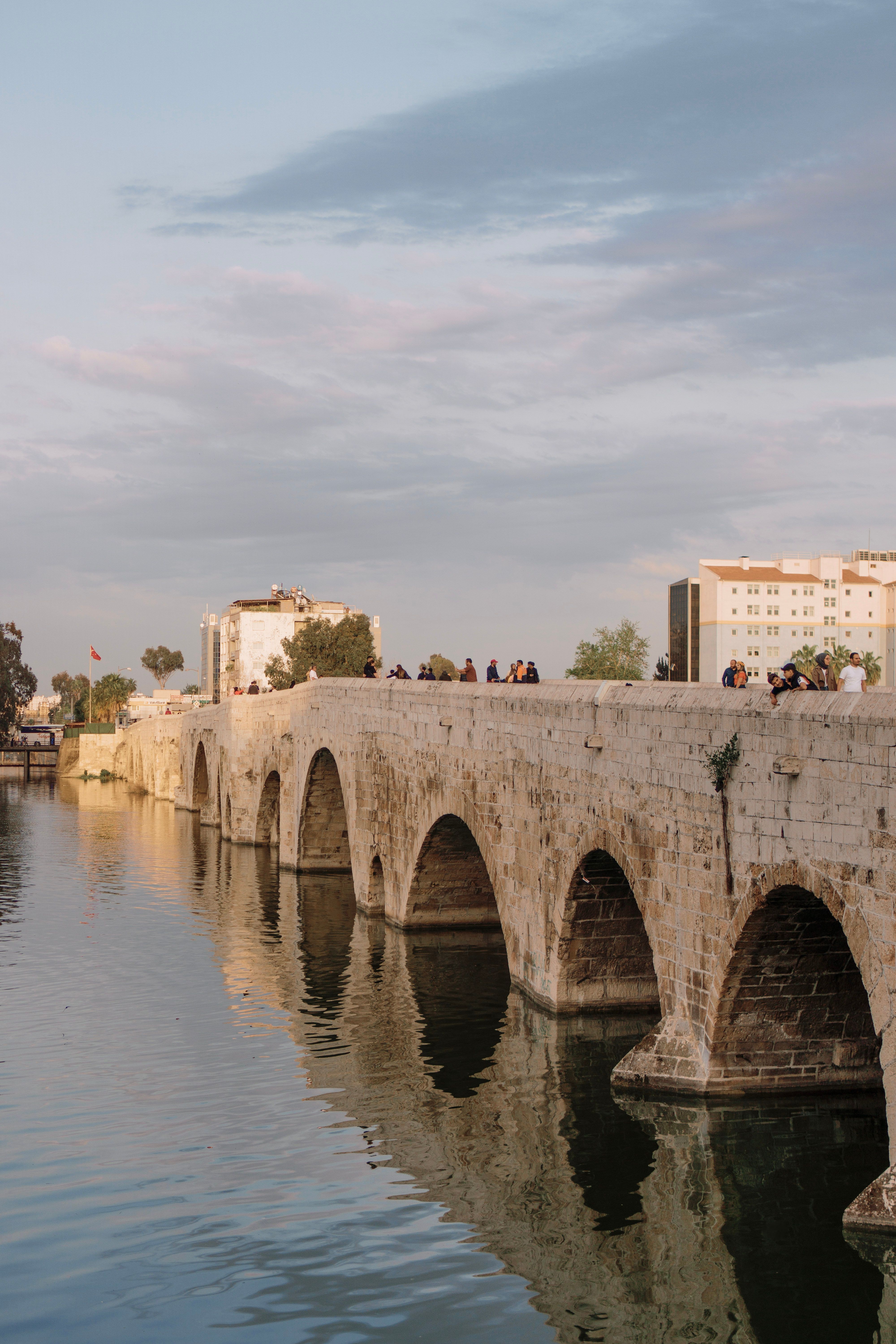 Scenic view of the ancient Taşköprü Bridge in Adana with people strolling, captured during a peaceful evening.