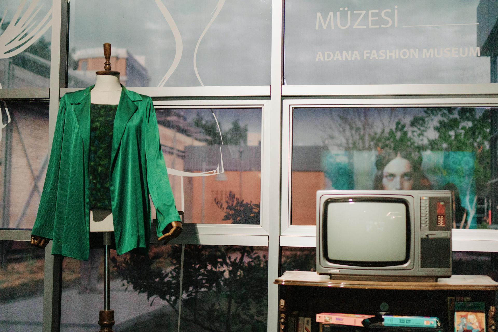 A mannequin with a green coat next to a retro TV at Adana Fashion Museum.
