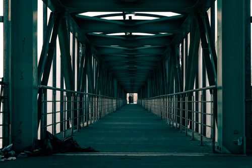 Free Long covered bridge pathway with a person silhouetted at the end, showcasing geometric patterns. Stock Photo