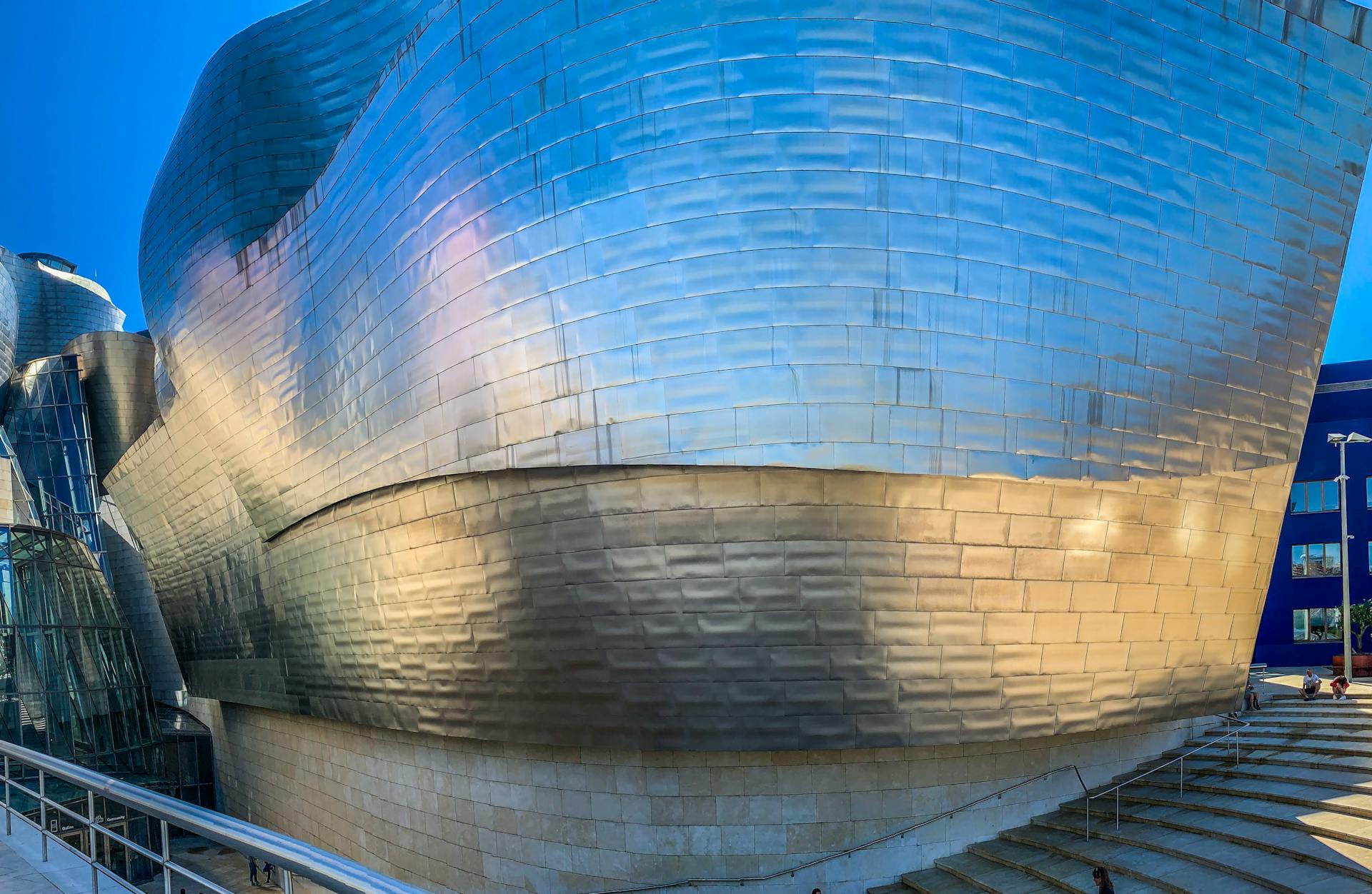 Sleek metallic facade of the Guggenheim Museum in Bilbao. Iconic architecture under a clear blue sky.