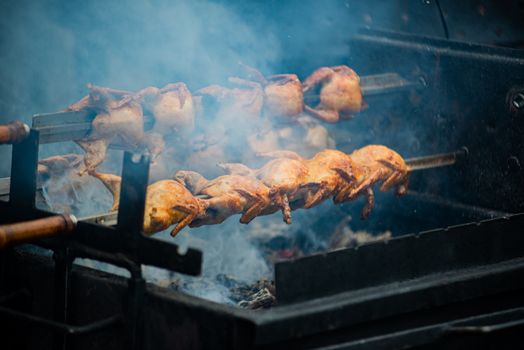 Juicy whole chickens roasting on a spit over open flames outdoors, creating smoky flavors.