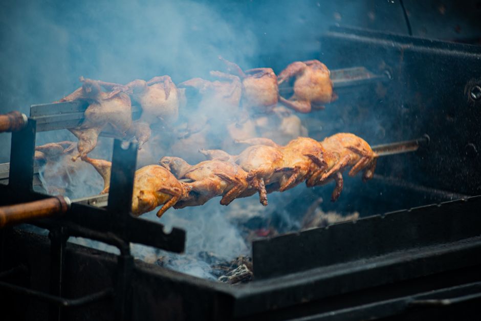 Juicy whole chickens roasting on a spit over open flames outdoors, creating smoky flavors
