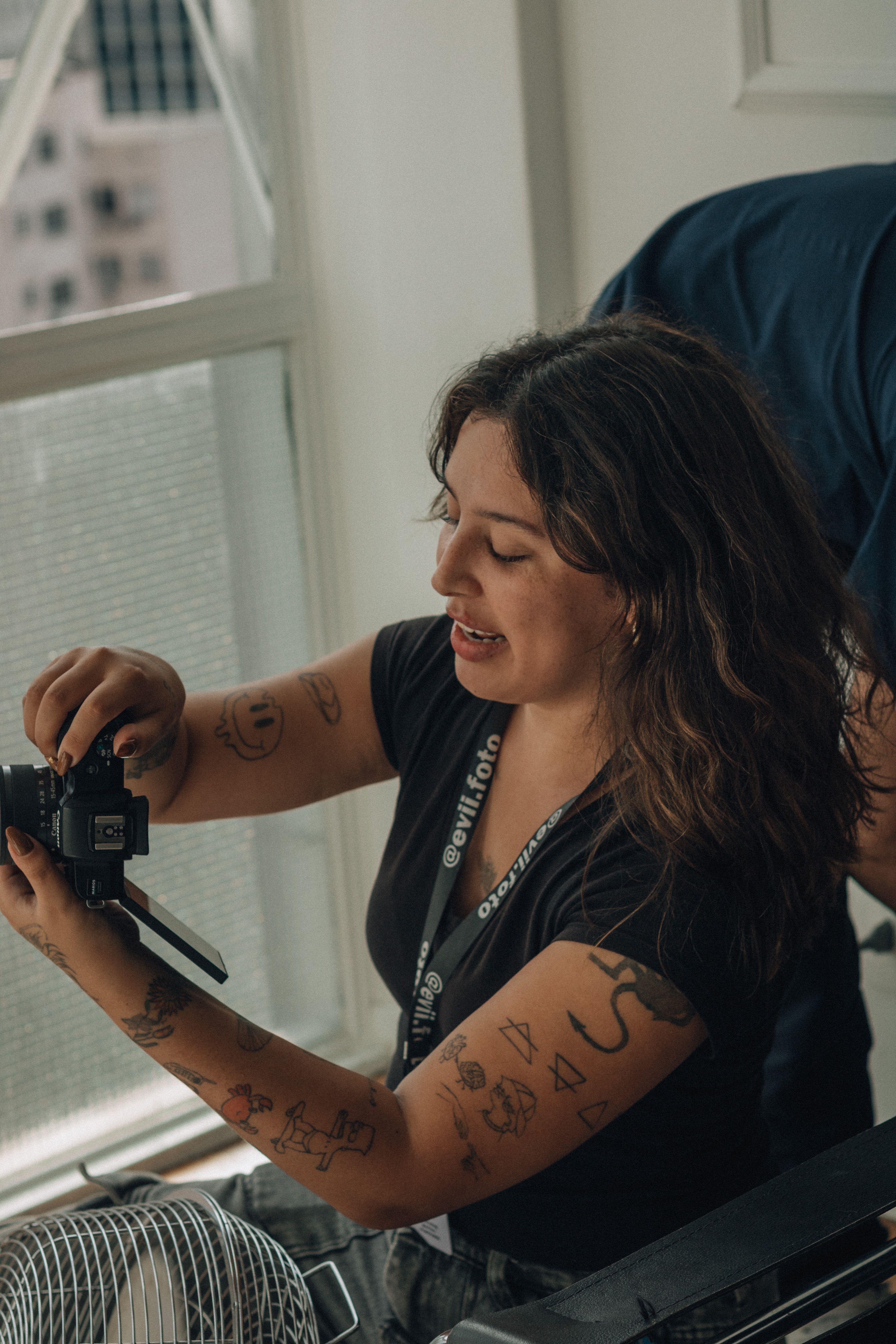 Portrait of a young tattooed female photographer adjusting her camera by a window.