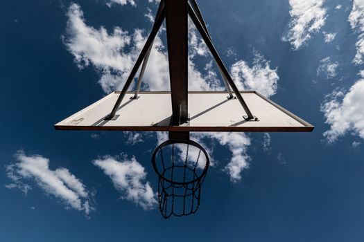 Low angle view of a basketball hoop and backboard with a vibrant blue sky and clouds.