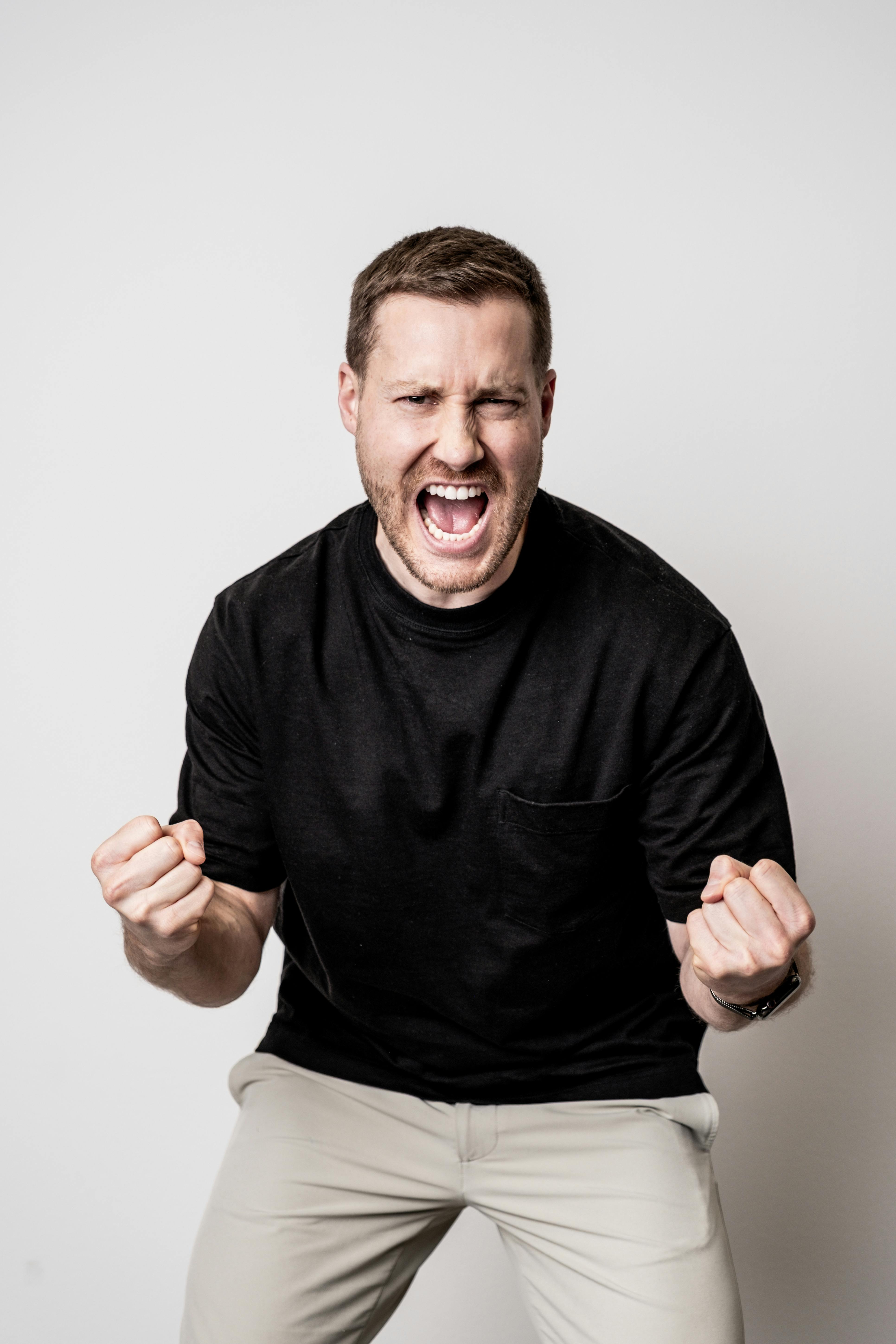 Energetic young man shouting with joy and enthusiasm in a simple studio setting.