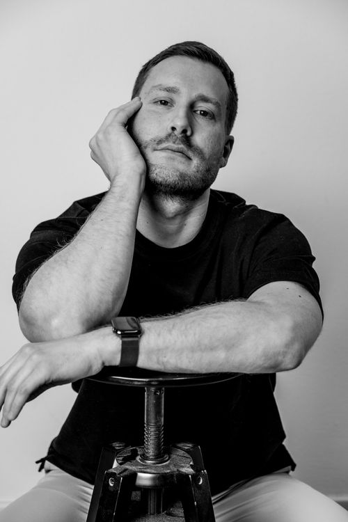 Free Black and white portrait of a man resting on a stool, wearing a watch, in a contemplative pose. Stock Photo