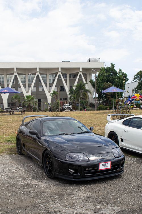 Free Two classic sports cars on display at an outdoor event in Jamaica, featuring an architectural building in the background. Stock Photo