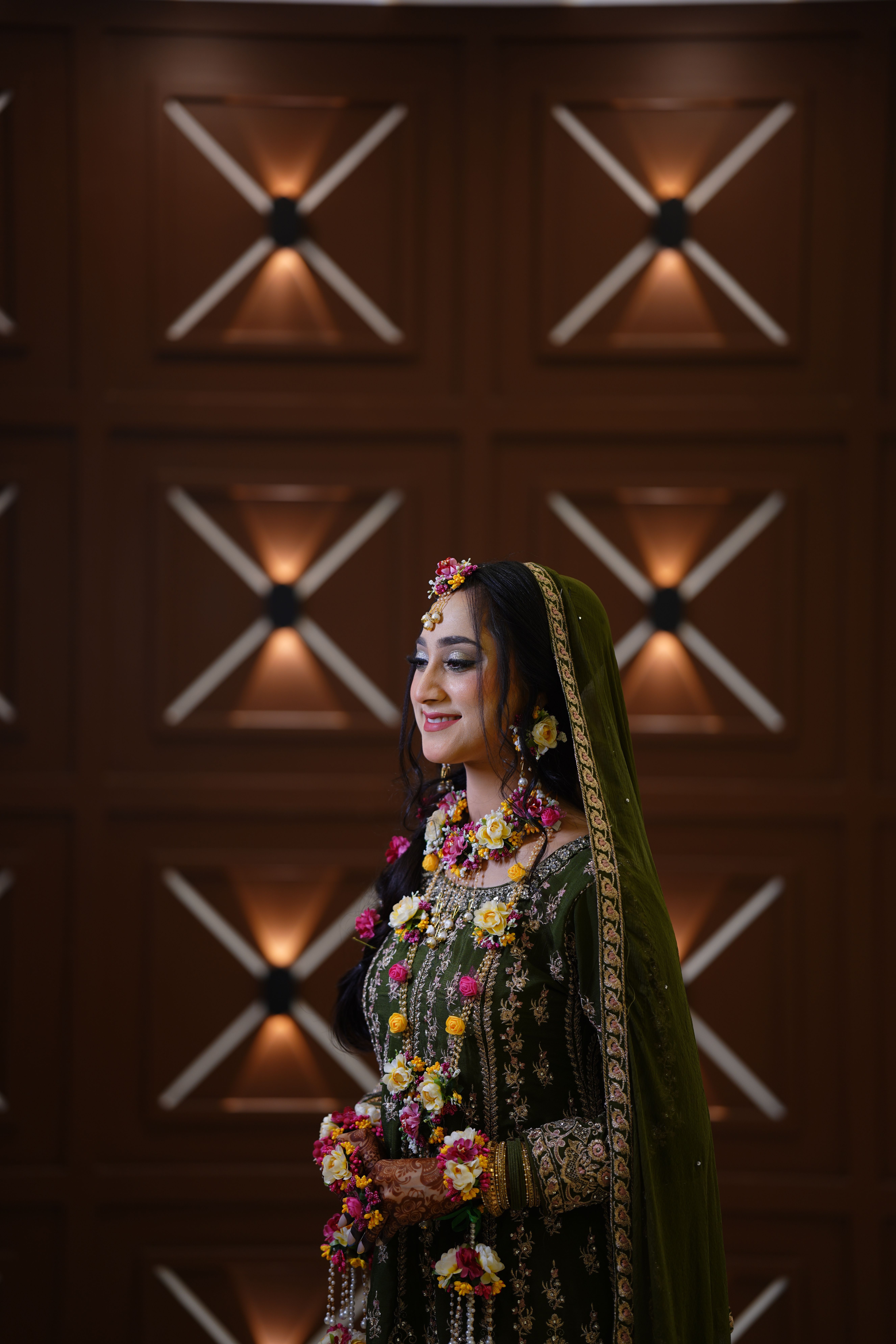 A beautifully adorned bride standing indoors at a night wedding ceremony.