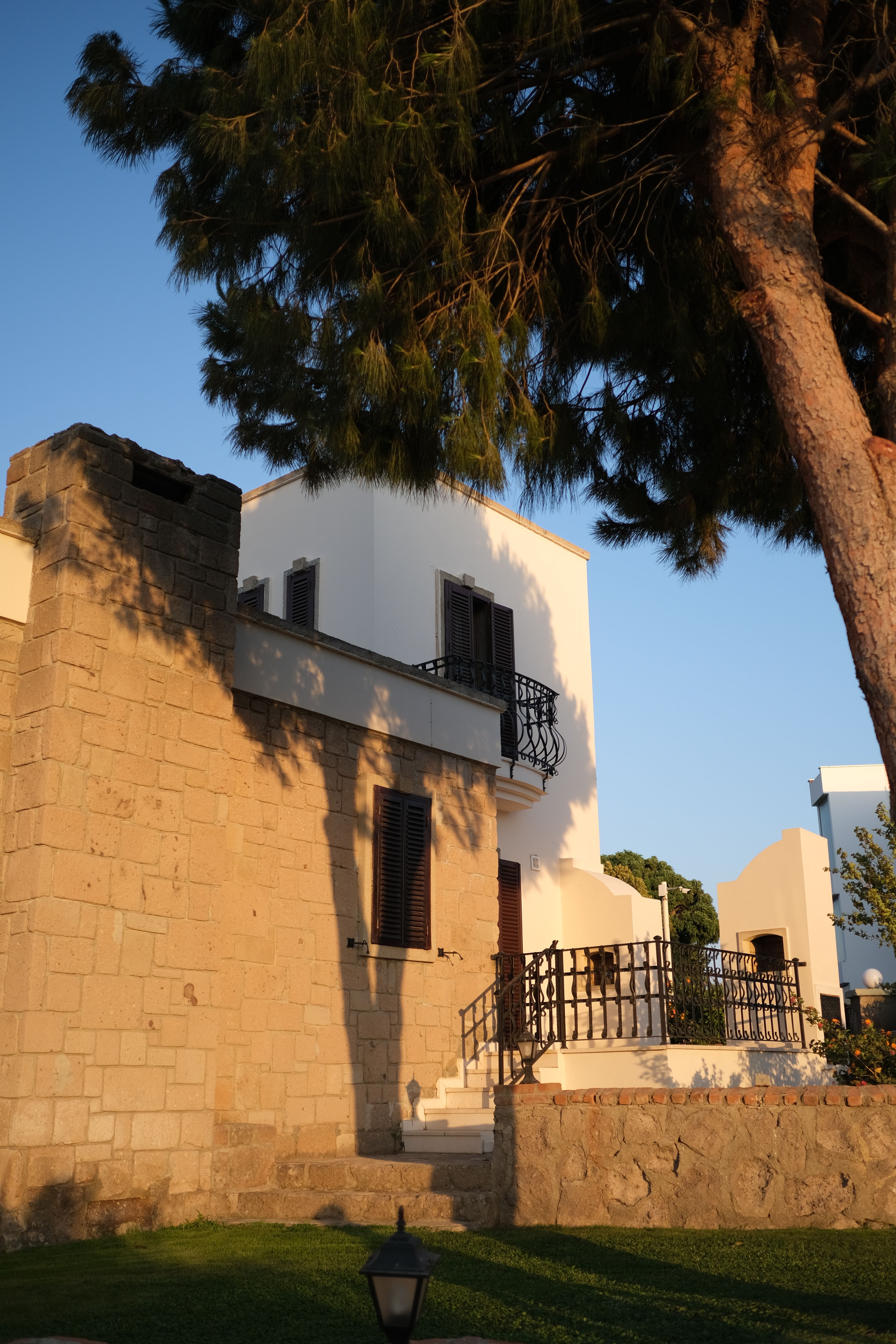 Charming Mediterranean villa with rustic stone walls and surrounding pine trees in soft evening light.