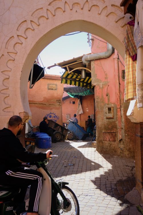 Free Colorful street scene in a Moroccan alleyway featuring a traditional arch and lively local activities. Stock Photo