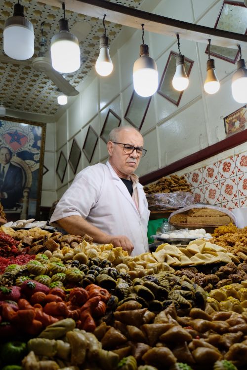 Free Man in a pastry shop surrounded by traditional sweets and desserts under warm lighting. Stock Photo