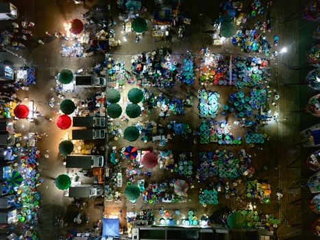 A vibrant aerial view of a bustling outdoor market at night with colorful umbrellas and lights.