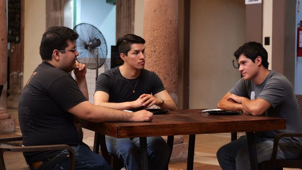 Three men having a casual conversation at an indoor table in Guanajuato, Mexico.