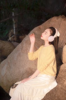 Woman in yellow sweater and white skirt enjoys sunlight outdoors, wearing headphones.