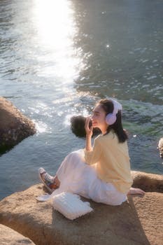 Young woman relaxing by the water with headphones, basking in the sunlight.