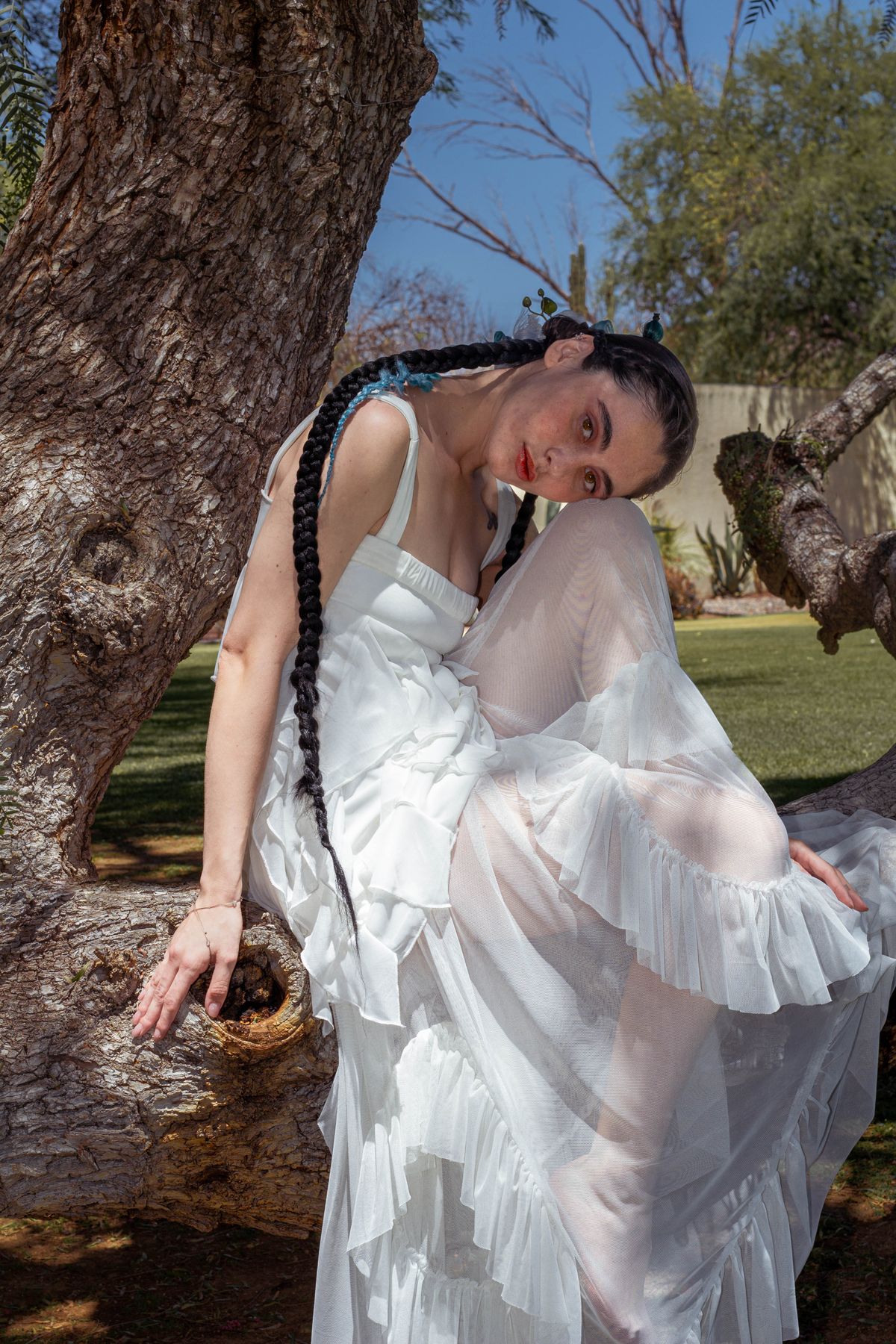 An elegant woman in a long white dress resting on a tree limb in a garden