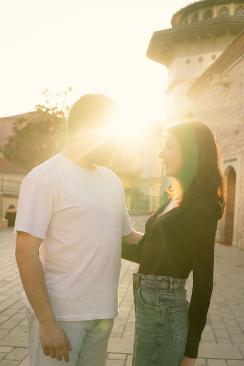 Free A couple standing close under the sun, evoking romance and warmth in an old town. Perfect for love-themed content. Stock Photo