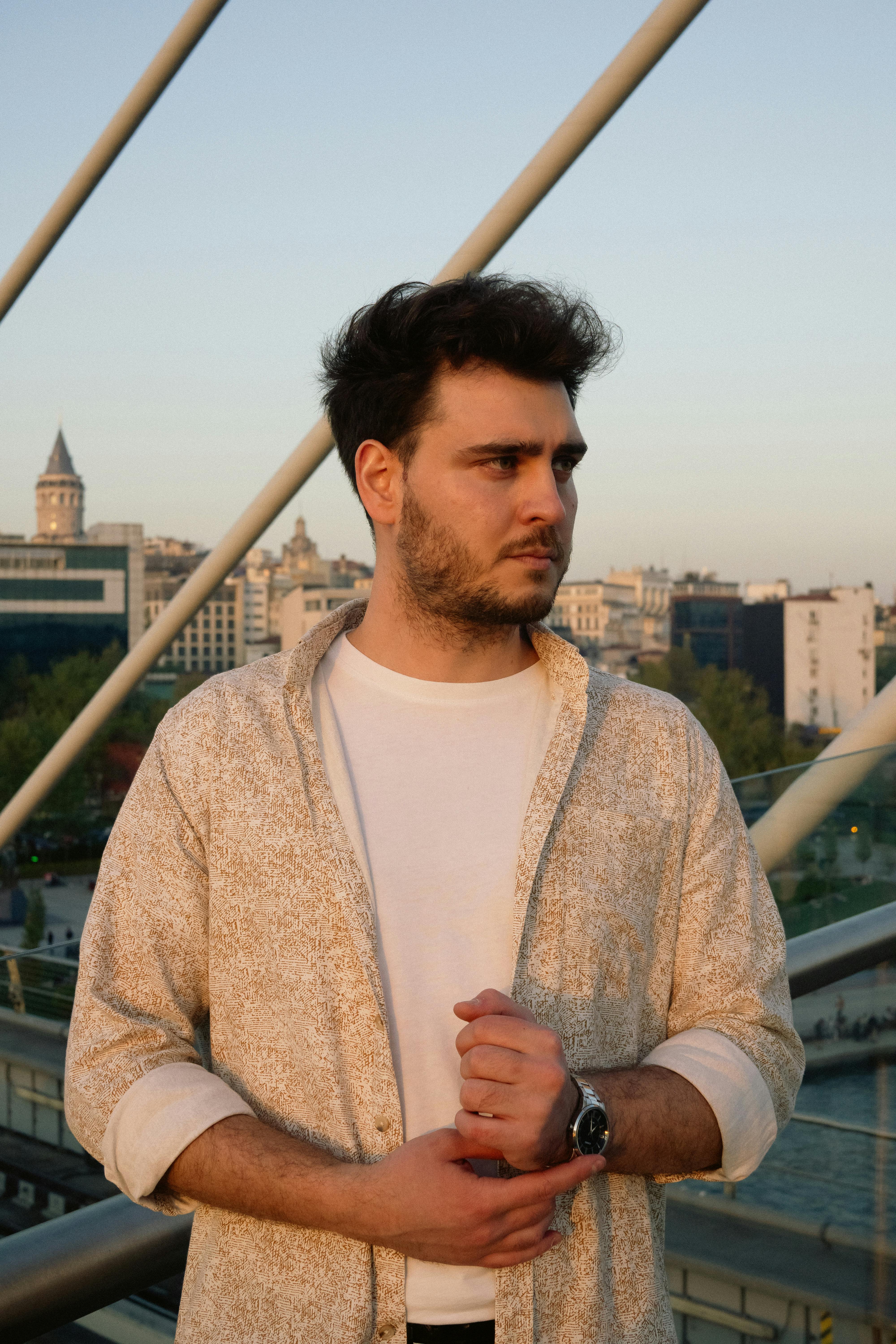 Young man in casual attire on a bridge with city backdrop during sunset.