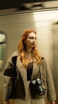 Woman with camera stands on a subway platform, train in motion.