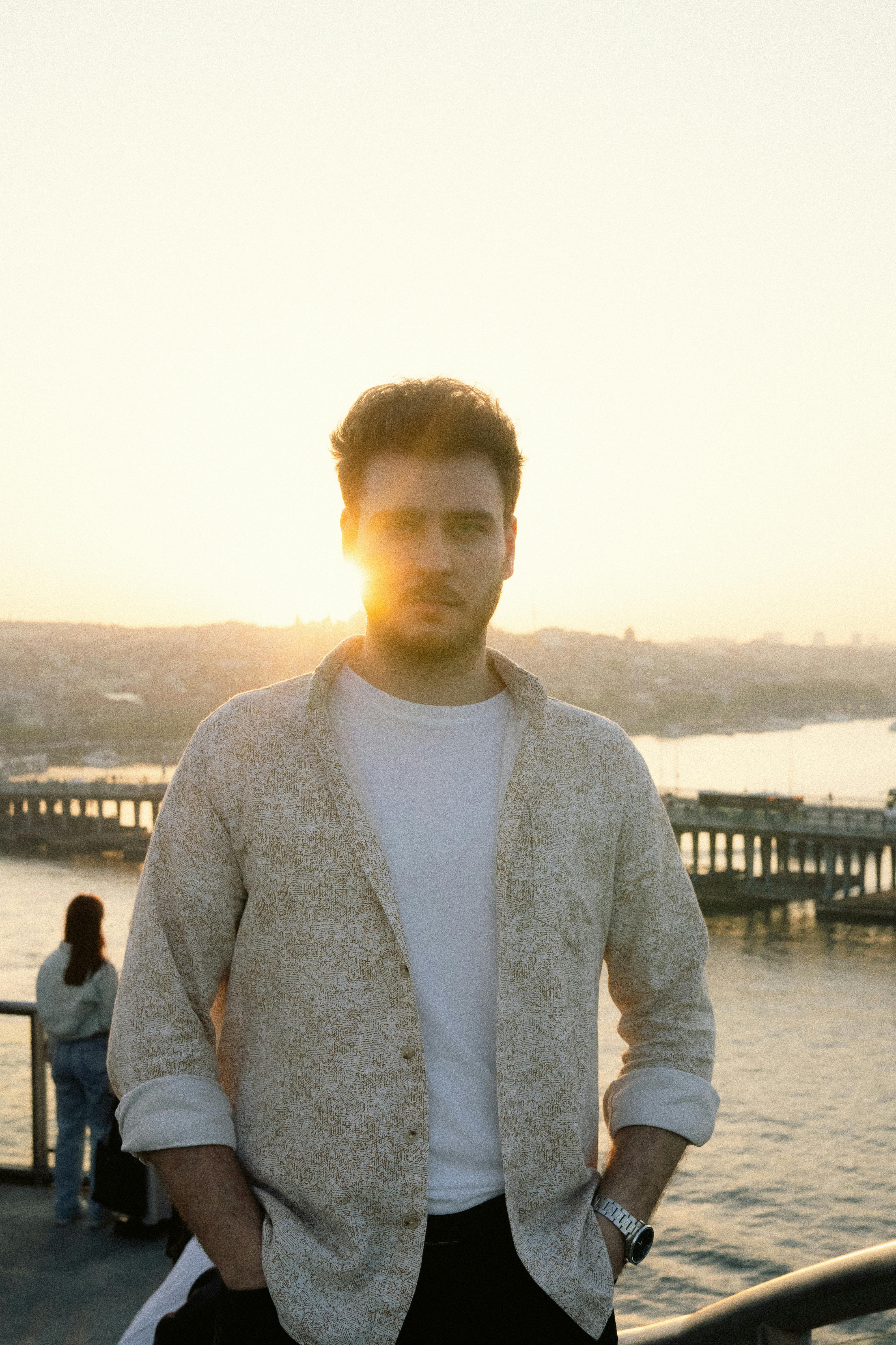 Man standing by the river at sunset with city skyline in the background.