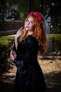 Redhead woman in a gothic dress with a floral headband poses in an outdoor setting.