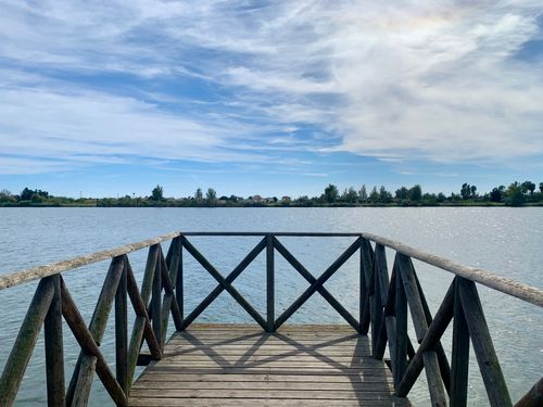 Free A serene view from a wooden pier overlooking a calm lake and clear sky. Stock Photo