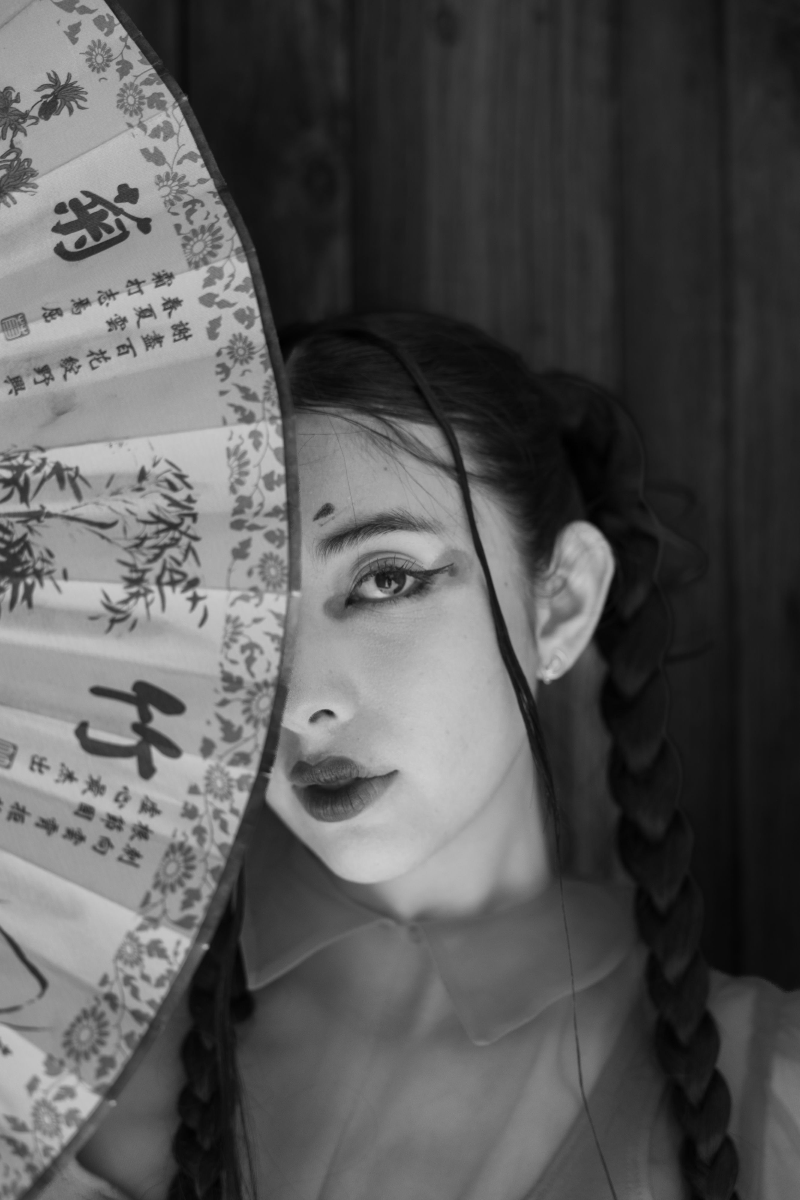 Black and white portrait of a woman partially hidden behind a Chinese fan.