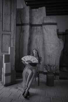 Artistic black and white photo of a woman with a fan in an industrial setting. Moody and elegant.