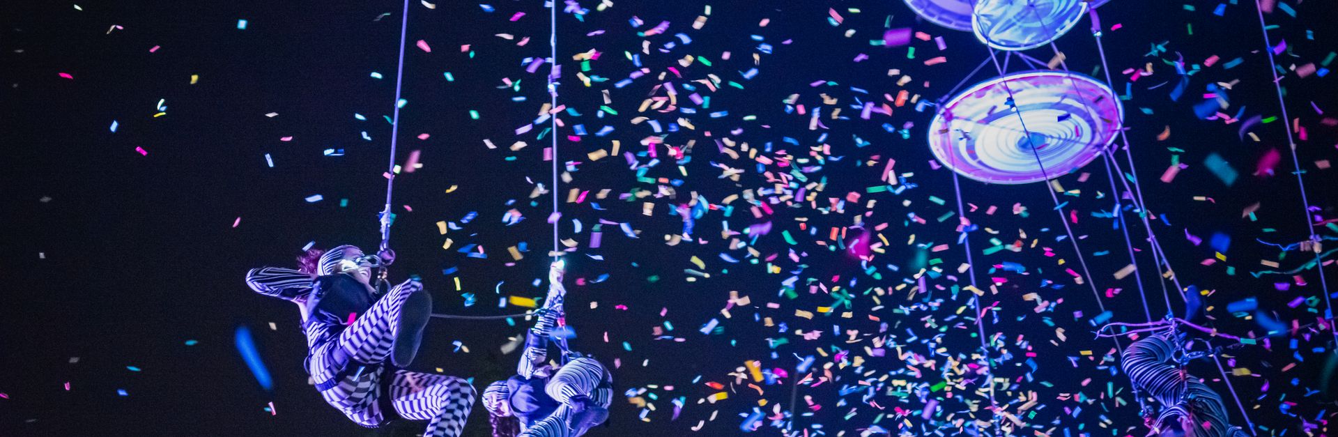 Colorful aerial acrobats performing at night with confetti shower, capturing festival magic in Merid