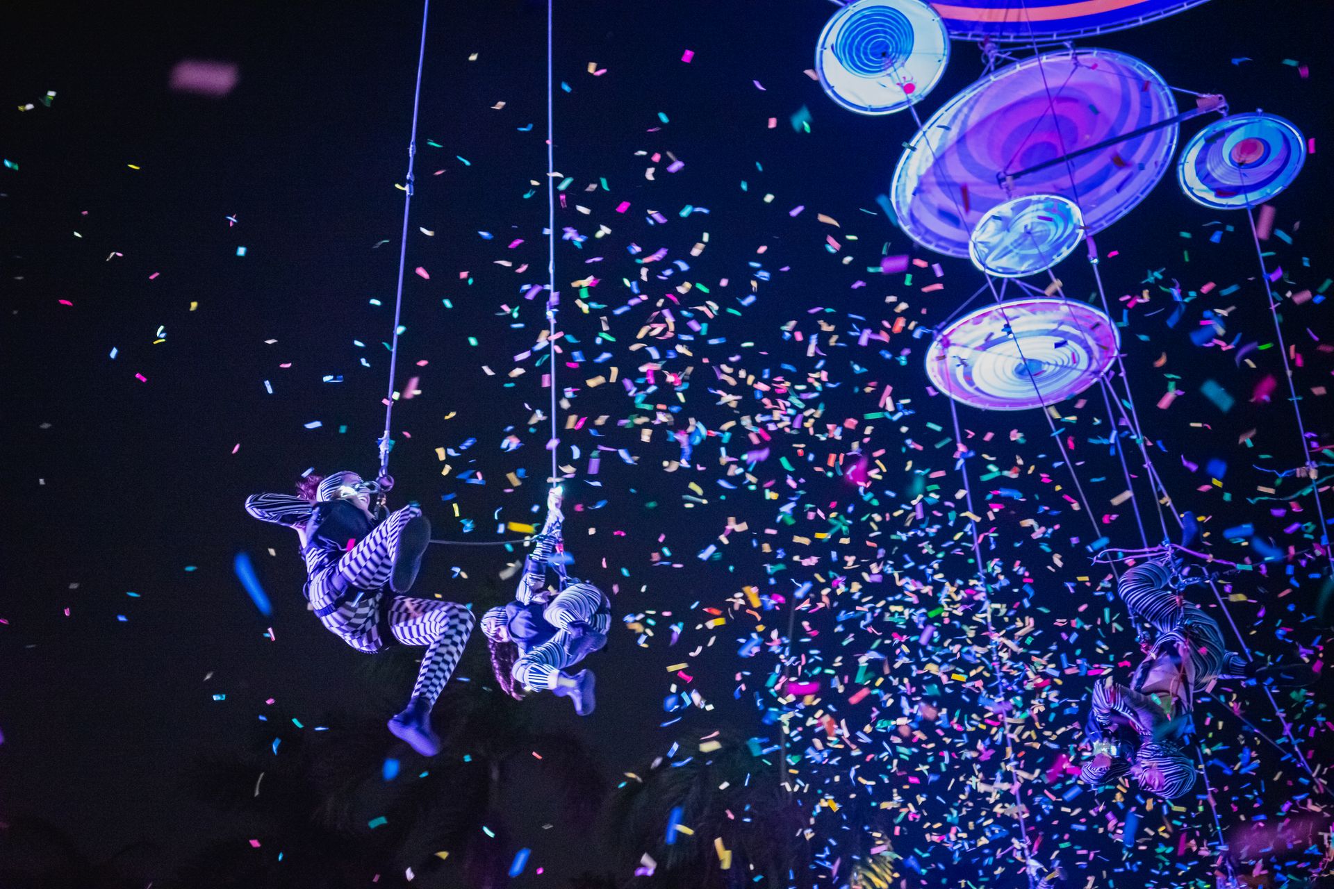 Colorful aerial acrobats performing at night with confetti shower, capturing festival magic in Merid