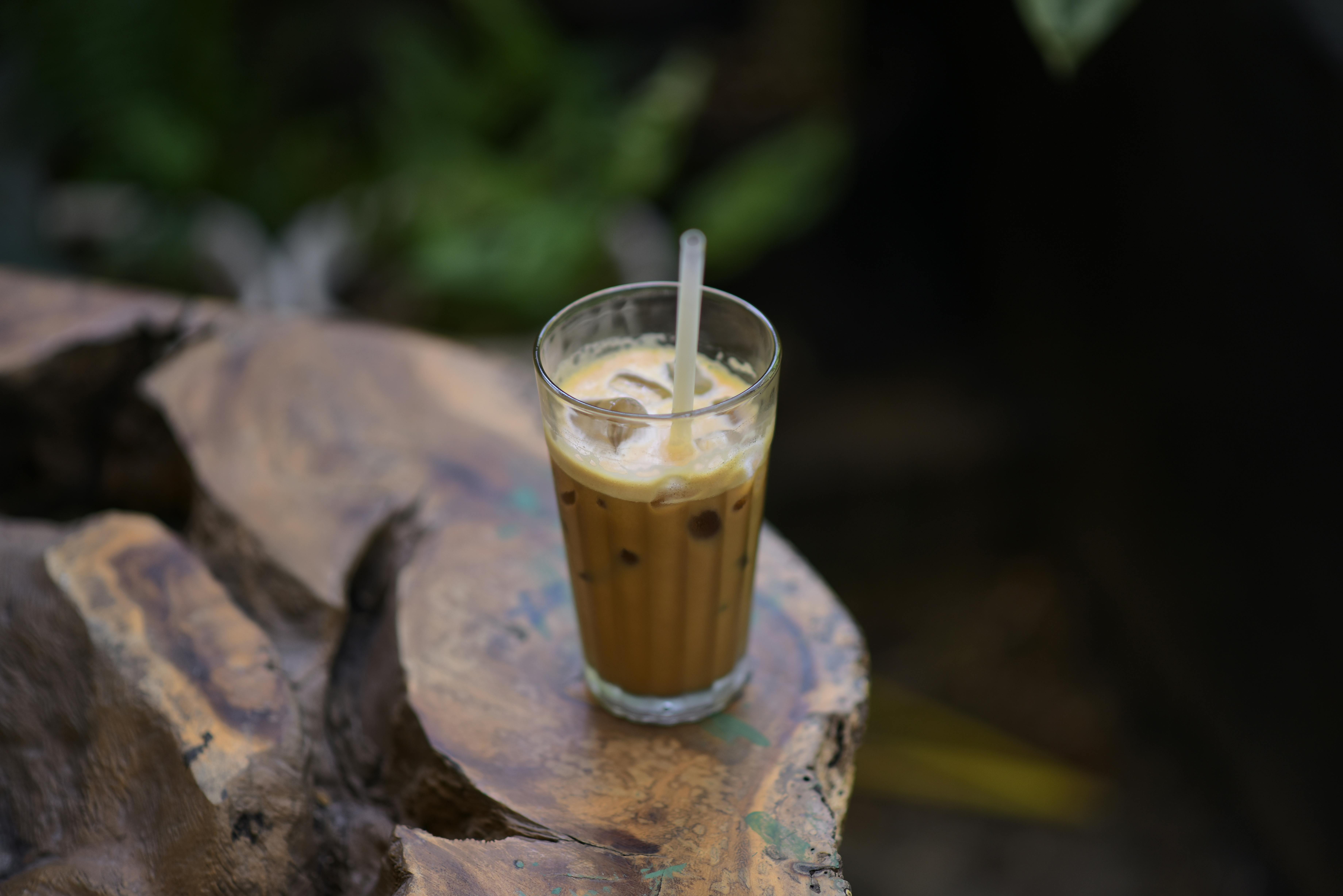 Glass of iced coffee with straw on rustic wooden table in an outdoor setting.