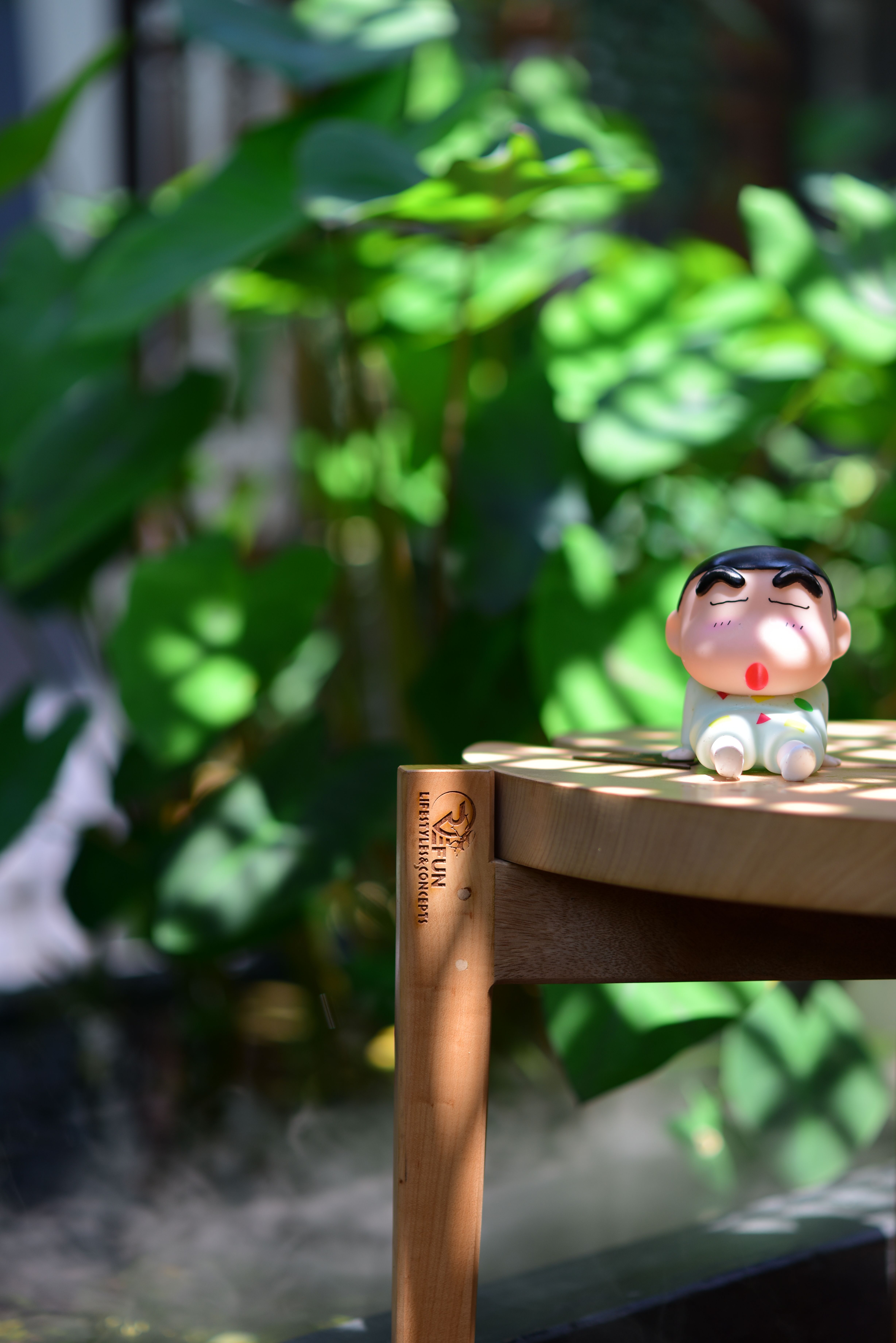 Bright scene of a toy figure on a wooden stool set against lush green plants.